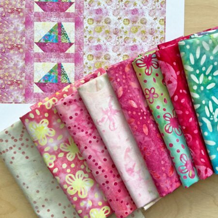 Top US quilting blog & shop, Kate Colleran Designs, shares about a sailboat quilt pattern Sail Away and a cute batik crib quilt! Image is of a pink sailboat quilt on paper with fabrics in front.