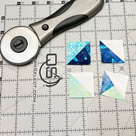 Top US quilting blog and shop, Kate Colleran Designs, shares her January Quilt Block Remix Challenge reveal. Image shows a cutting mat, rotary cutter and half square triangle units in white and blue batik fabrics.