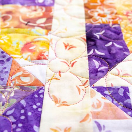 Top US quilting blog and shop, Kate Colleran Designs, shares about her new batik fabric line Winged Things and a FQ giveaway! Image is closeup of the quilting of a flower in variegated thread on yellow, white, purple and orange batiks.