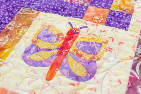 Top US quilting blog and shop, Kate Colleran Designs, shares about her new batik fabric line Winged Things and a FQ giveaway! Image is an appliquéd butterfly quilt block block in purple, orange and  yellow batiks.