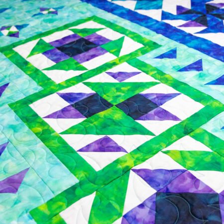 Top US quilting blog and shop, Kate Colleran Designs, shares about her new block of the month quilt using Aura fabrics from QT! Image is a closeup of quilt blocks in mottled purple, green and dark blue fabrics.
