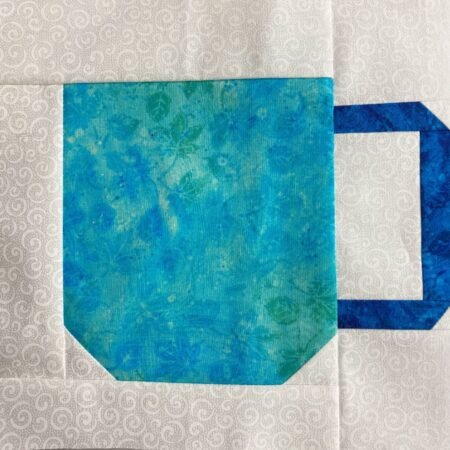 Top US quilting blog and shop, Kate Colleran Designs, shares a free quilt block pattern and shares about an upcoming QAL! Image is a coffee cup quilt block in blue and white fabrics.