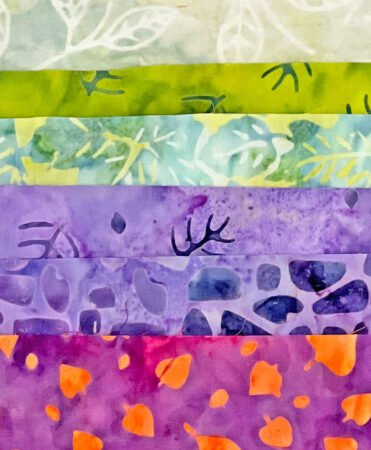 Top US quilting blog and shop, Kate Colleran Designs, shares about the June quilt block remix and the Monkey Wrench quilt block. Image is of batik fabrics in greens, purples and magenta.