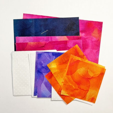 Top US quilting blog and shop, Kate Colleran Designs, shares tips in the Allure BOM Block 7 post. Image is a stack of fabrics cut as squares and rectangles in mottled bright purple, magenta pink, orange and white.