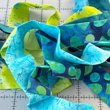 Top US quilting blog and shop, Kate Colleran Designs, shares about the Bias Tape Challenge and her project that she created. Image is a closeup of blue and green batik strips in a pile.