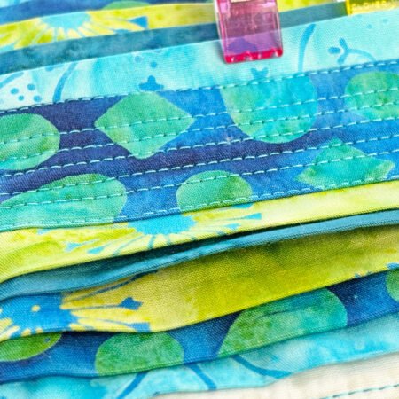 Top US quilting blog and shop, Kate Colleran Designs, shares about the Bias Tape Challenge and her project that she created. Image is a closeup of blue and green batik strips sewing together.