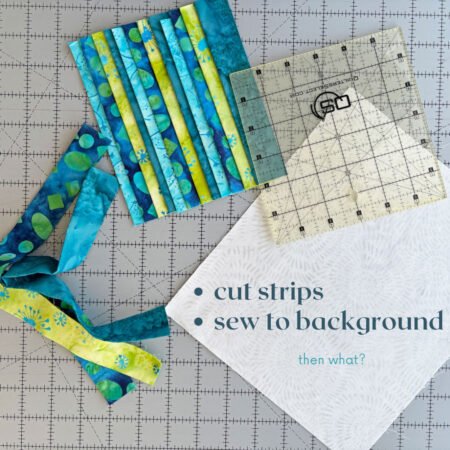 Top US quilting blog and shop, Kate Colleran Designs, shares about the Bias Tape Challenge and her project that she created. Image is a closeup of blue and green batik strips, a white background and ruler read for sewing together.