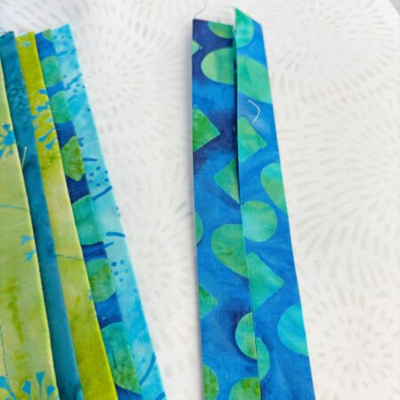 Top US quilting blog and shop, Kate Colleran Designs, shares about the Bias Tape Challenge and her project that she created. Image is a closeup of blue and green batik strips laid out.