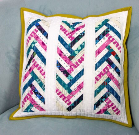 Top US quilting blog and shop, Kate Colleran Designs, shares about her book Patchwork Braids and using pieced strips in a braid. Image is a pillow with pink and blue fabric braids with white. 