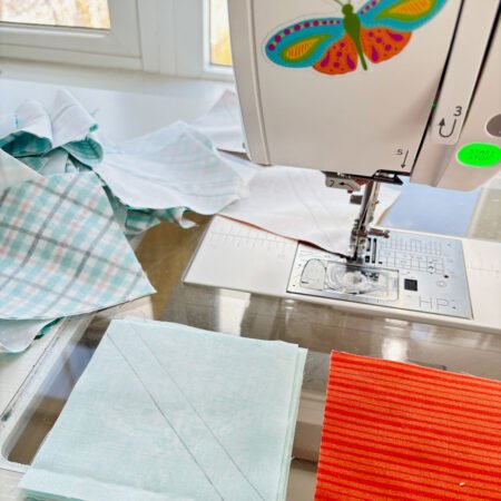 Top US quilting blog and shop, Kate Colleran Designs, shares about her new Chalk Hill Blue quilt pattern! Image is a close up of a sewing machine and chain piecing HST units in teal, white and orange.