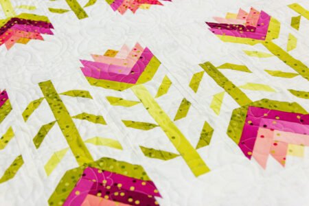Top US quilting blog and shop, Kate Colleran Designs, shares about her book Patchwork Braids and using pieced strips in a braid. Image is a close-up of pieced braid flowers in pink and green ombre fabric on white.