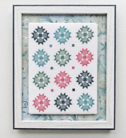 Top US quilting blog and shop, Kate Colleran Designs, shares about her Christmas in July posts and a last giveaway for the month! Image is star quilt blocks made as cross stitch in blues, grey greens and rose in a white wood frame.