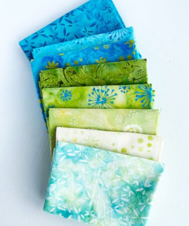 Top US quilting blog and shop, Kate Colleran Designs, shares about a quilt from Patchwork Braids and tips on recoloring a quilt. Image is a row of blue and green batik FQs.