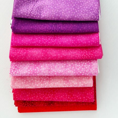 Top US quilting blog and shop, Kate Colleran Designs, shares about a quilt from Patchwork Braids and tips on recoloring a quilt. Image is a stack of pink, red and purple FQs with spots.