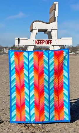 Top US quilting blog and shop, Kate Colleran Designs, shares about a quilt from Patchwork Braids and tips on recoloring a quilt. Image is a blue and orange braid quilt hanging on a lifeguard chair at the beach.