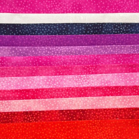 Top US quilting blog and shop, Kate Colleran Designs, shares about a quilt from Patchwork Braids and tips on recoloring a quilt. Image is a flat shot of pink, red, purple, blue and white fabrics with spots.