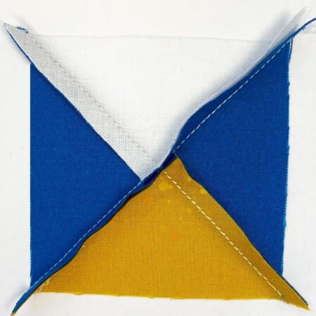 Top US quilting blog and shop, Kate Colleran Designs, shares about the Jingle Bell Pines Block Party Block 7 Rose Star. Image is the back of a quarter square triangle unit in blue, white and gold with center seam unpressed.