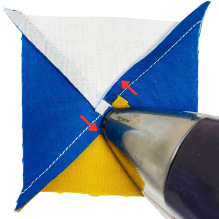 Top US quilting blog and shop, Kate Colleran Designs, shares about the Jingle Bell Pines Block Party Block 7 Rose Star. Image is the back of a quarter square triangle unit in blue, white and gold with the tip of an iron pressing the swirled seams. Red arrows show the direction to press.