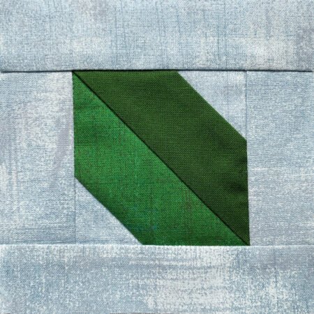 Top US quilting blog and shop, Kate Colleran Designs, shares about the Jingle Bell Pines BOM Block Party setting blocks and borders. Image is a piece simple leaf quilt block with 2 greens and a light blu ebackground.