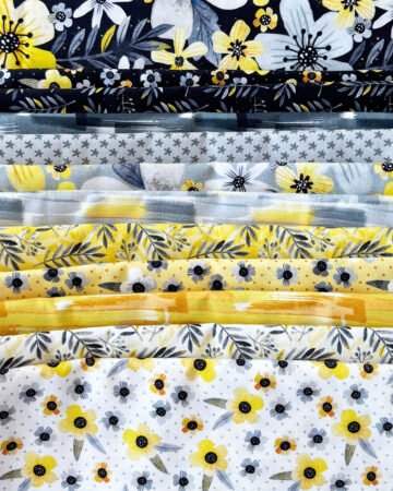 Top US quilting blog and shop, Kate Colleran Designs, shares about her quilt Gemstone and the quilt remake in Blissful Blooms. Image is a line of fabrics in black, white, yellow and grey with flowers, abstracts and leaves.
