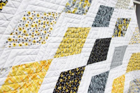 Top US quilting blog and shop, Kate Colleran Designs, shares about her quilt Gemstone and the quilt remake in Blissful Blooms. Image is a yellow, grey and black and white quilt closeup with geometric quilting.