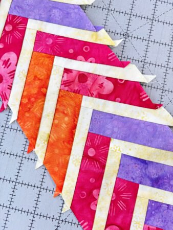 Top US quilting blog and shop, Kate Colleran Designs, shares about her 2026 temperature quilt and the braid blocks she will use! Image is a row of pink, purple and orange braids pieces sewn together with a light skinny braid in between.