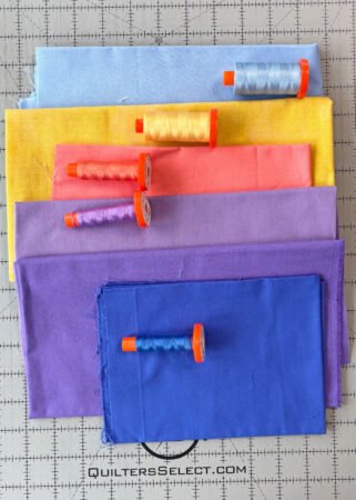 a stack of solid fabrics in light blue, yellow, coral, lavender, purple and royal blue with matching spools of thread.