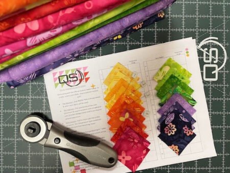 Top US quilting blog and shop, Kate Colleran Designs, shares about her 2026 temperature quilt and the braid blocks she will use! Image is a paper temperature tracker with fabric squares shown on top and bolts of pink, orange, green and purple fabric bolts off to the side