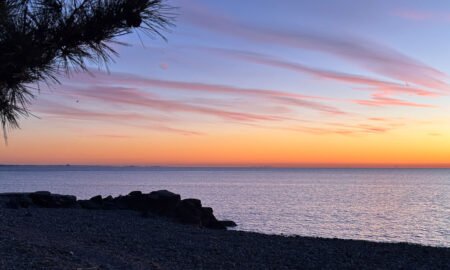 photo of a sunset over the water in blues, yellow, coral, purple and black in the foreground.