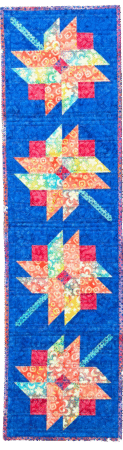 Petal Party is a table runner with a deep blue background and flower shapes made a a print fabric with orange and red petals and aqua stems
