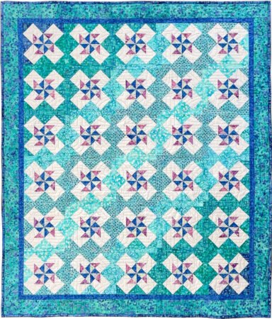 Rotationals quilt with pinwheels and diagonal bands of gradation of colors in blues, aqua and teals with a aqua and blue print border