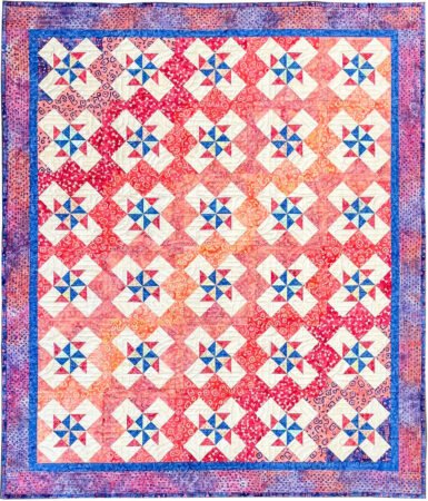 Rotationals quilt with pinwheels and diagonal bands of gradation of colors in blues, oranges, reds with a red and blue print border