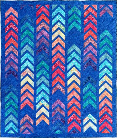 UpTick braid quilt with chevron shapes in reds, oranges, cream, aqua, and teals with areas of deep blue and deep blue borders